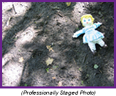 Child's doll laying in the dirt on a shadowed forest floor (Professionally Staged Photo).